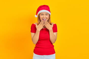 Portrait of young Asian woman wearing Christmas hat with surprised facial expression over yellow background