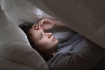 a woman lying in bed at night uses a phone, surfing the Internet at night, insomnia and addiction...