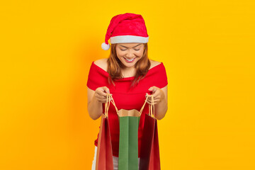 Smiling young Asian woman opening and looking inside shopping bag on yellow background