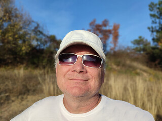 portrait of a smiling man in sunglasses and a cap in nature