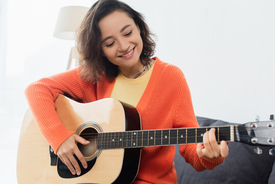 happy young woman playing acoustic guitar at home.