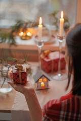 a woman in a red plaid dress and with a bow clip on her head holds a packed gift for the new year or birthday. view from the back. Christmas mood and the spirit of winter. gifts and surprises for