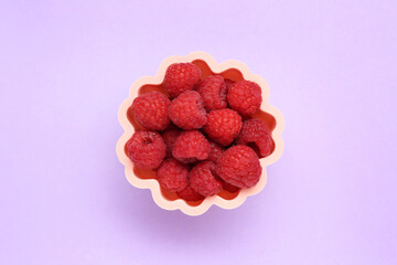 Bowl of fresh delicious raspberries on violet background, top view