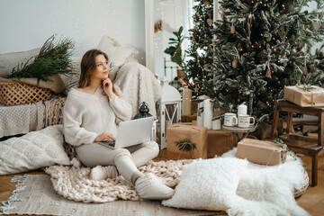  smiling young caucasian woman in warm winter clothes looking at computer tablet scree, reading Christmas wishes or congratulating friends with New Year night online in social network.