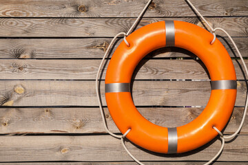 Orange life buoy hanging on wooden wall, space for text