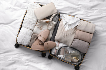 Open suitcase with folded clothes, shoes and accessories on bed, top view