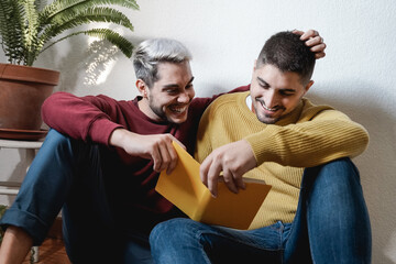 Lgbt gay couple hugging and reading book together indoor at home - Homosexual love and romance concept