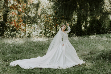 Fototapeta na wymiar Bride in a green forest in an amazing dress. The veil flutters in the air