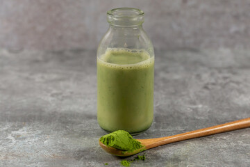 A scoop of matcha powder and a matcha latte against a grey background