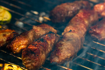 Grilling meat rolls called mici or mititei with vegetables on char barbecue. Charcoal grill with...