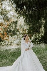The bride in a beautiful white dress stands in front of a tree