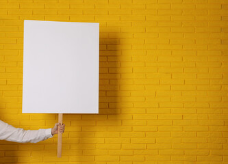 Woman holding blank sign near yellow brick wall, closeup. Space for design