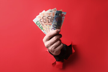 Businessman breaking through red paper with money in hand, closeup