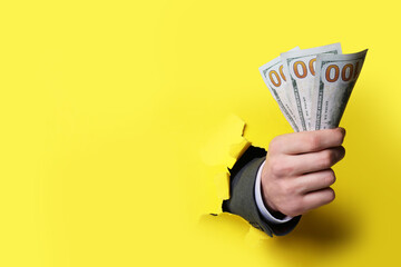 Businessman breaking through yellow paper with money in fist, closeup. Space for text
