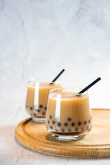 Two glasses with milk bubble tea with delicious tapioca pearls on wooden board. Famous Taiwan milk jelly tea. Trendy drinks with copy space.