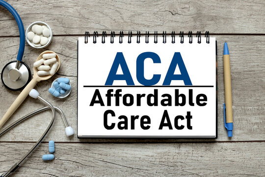 ACA AFFORDABLE CARE ACT. Medical stethoscope blue and white blue pills and notepad on a wooden table with place for text. Flat view.