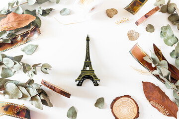 Eiffel tower, old-fashioned camera films, dried branches of eucalyptus leaves, and wood pieces on white background. Flat lay, overhead view, top view. Vintage frame composition.