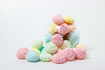 Multicolored meringues on a white background. Glass vase overflowing with multicolored meringues.