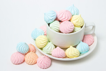 Multicolored meringues on a white background. A teacup overflowing with multicolored meringues.