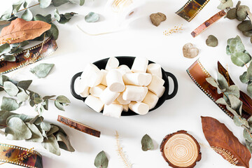 Marshmallows and frame with  old-fashioned camera films, dried branches of eucalyptus leaves, and wood pieces on white background. Flat lay, overhead view, top view. Vintage composition.
