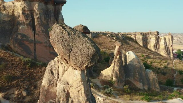 Drone flying close around beautiful mysterious tall rocks with big stones on top near small town in Cappadocia Turkey.