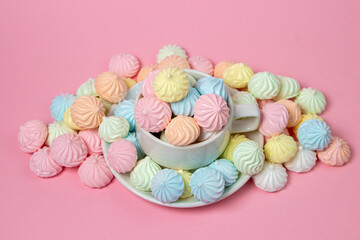 Multicolored meringues on a pink background. A teacup overflowing with colored meringues.