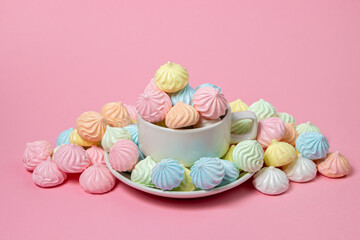 Multicolored meringues on a pink background. A teacup overflowing with colored meringues.