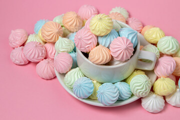 Multicolored meringues on a pink background. A teacup overflowing with colored meringues.