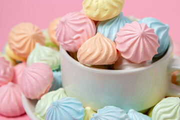 Multicolored meringues on a pink background. A teacup overflowing with colored meringues.