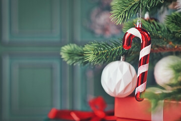 Candy cane christmas ornament on tree with gifts on side of green background