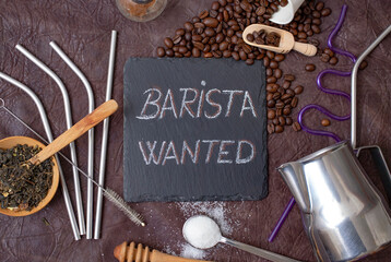 barista wanted written with chalk on a black stone tile, surrounded by coffee, tea, sugar and bartender utensils 