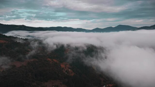 Aerial footage of misty fog over mountain village. Morning autumn landscape, mountain range peak over haze clouds on highland hills. Nature background. Beautiful wild landscape. Cinematic drone flight