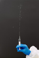 hand in a blue medical glove holding syringe spraying medicine on a dark grey background