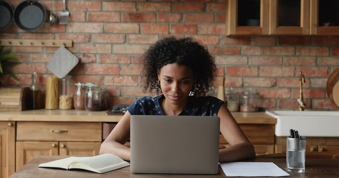 Pensive African woman sit at table with laptop staring looking into distance, distracted from telecommute computer work, consider creating new ideas or looks for inspiration. Online freelance concept