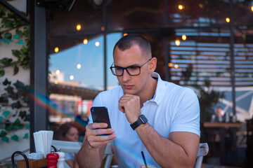 Young handsome businessman eating in a restaurant while using smartphone