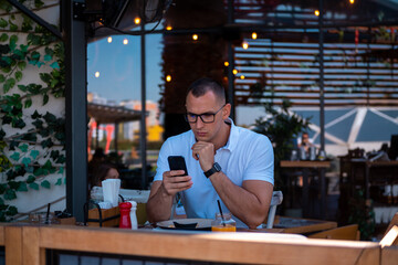 Young handsome businessman eating in a restaurant while using smartphone