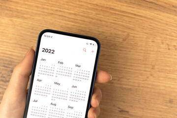 Calendar for 2022 on smartphone screen, close-up view. Wooden background. New year planning concept photo