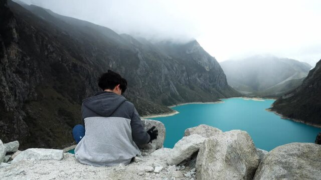 a young teenager sitting looking at the incredible turquoise lagoon Paron in Huaras with mist on the hills