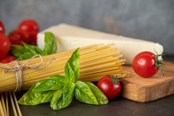 spaghetti on a dark background, cheese, tomatoes, and basil