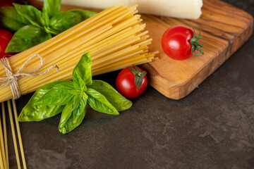 spaghetti on a dark background, cheese, tomatoes, and basil