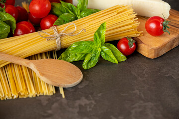 spaghetti on a dark background, cheese, tomatoes, and basil