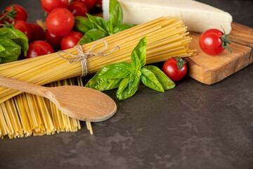 spaghetti on a dark background, cheese, tomatoes, and basil