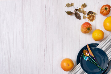 Autumn leaves, blue plates and iridescent silverware on a light wooden table