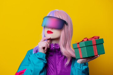 Style woman in VR glasses and 90s sport suit hold gift box on yellow background