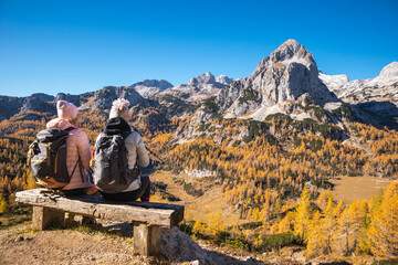 Two female hikers on a bench enjoying mountain panorama view on a sunny autumn day with golden...