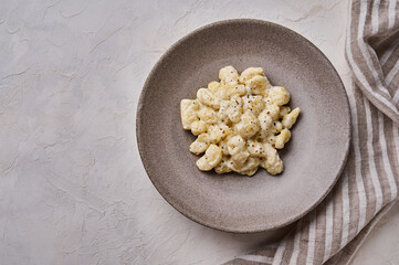 Homemade gnocchi, prepared with potato and whole grain flour dough with cream sauce on gray concrete background. Top view. Copy space