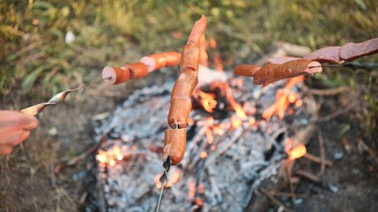 Sausages on twigs are fried over a fire.