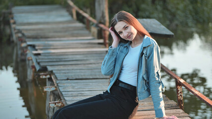 A young girl with long hair poses by the bridge on the river.