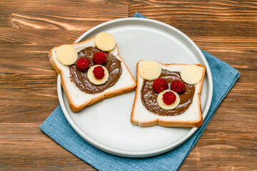 Funny bear face sandwich toast bread with peanut butter, cheese and raspberry on napkin wooden background close up. Kids child sweet dessert breakfast lunch food