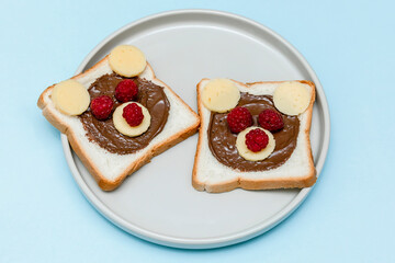 Funny bear face sandwich toast bread with peanut butter, cheese and raspberry on plate blue background. Kids child sweet dessert breakfast lunch food